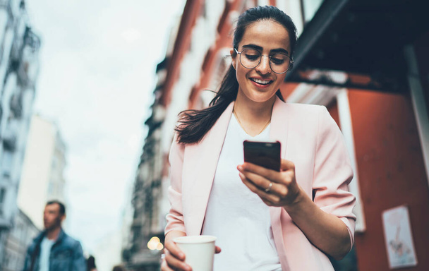 Joyful hipster girl enjoying network browsing during leisure time in urban town, happy Spanish blogger messaging with friends via modern smartphone using 4g wireless internet for web booking - Photo, image