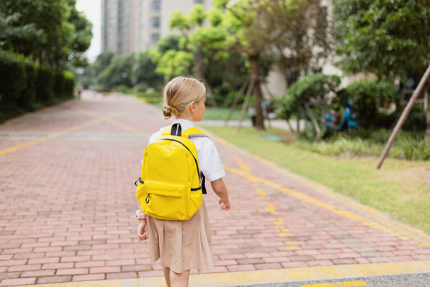 Schoolgirl back to school after summer vacations. Child in uniform standing early morning outdoor.  - Photo, Image