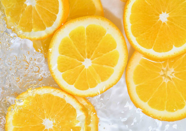 Πορτοκάλια close-up σε υγρό με φυσαλίδες. Φέτες από ζουμερά πορτοκάλια στο νερό. Κοντινό πλάνο φρέσκες φέτες πορτοκαλιού σε λευκό φόντο - Φωτογραφία, εικόνα