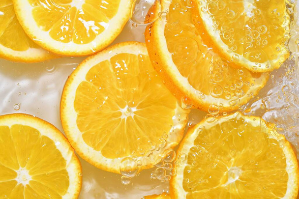Sinaasappels close-up in vloeistof met belletjes. Snijdt sappige sinaasappels in het water. Close-up verse schijfjes sinaasappels op witte achtergrond - Foto, afbeelding