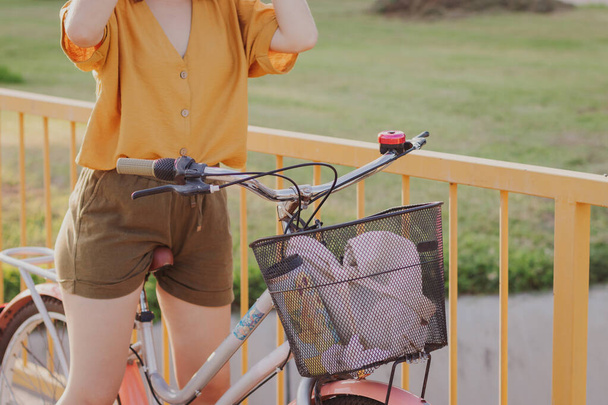 Mujer joven de pie en bicicleta en un parque sin valla de la cara en el fondo - Foto, imagen