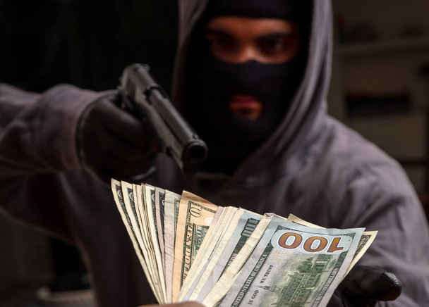 Robo a mano armada, ladrón con una pistola en la mano enguantada, hombre en un pasamontañas amenaza con un arma por robar dinero, vista de cerca. - Foto, imagen