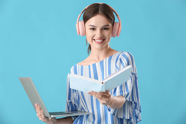 Young woman with laptop, book and headphones on color background - Fotoğraf, Görsel