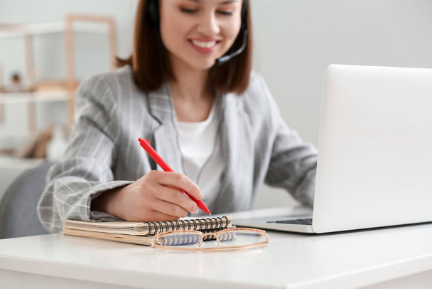 Jeune femme avec ordinateur portable écrivant quelque chose dans un cahier à la maison - Photo, image