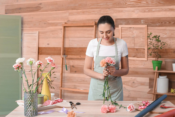 Γυναίκα ανθοπωλείο κάνει μπουκέτο με γαρύφαλλα λουλούδια στο εργαστήριο - Φωτογραφία, εικόνα