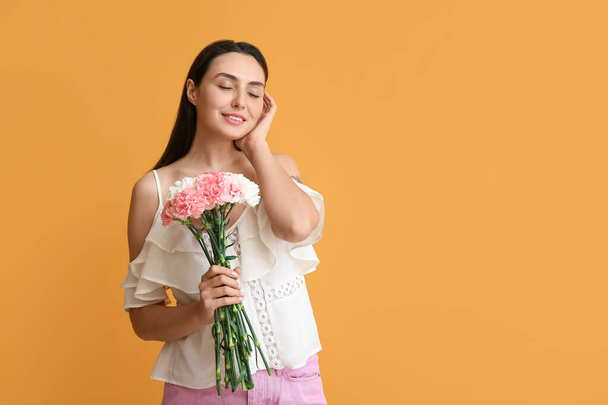 Mujer joven con hermosas flores de clavel sobre fondo de color - Foto, Imagen