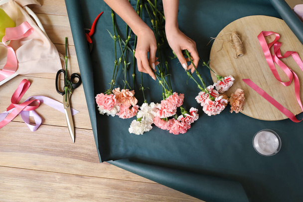 Female florist making bouquet with carnation flowers in workshop - Photo, Image