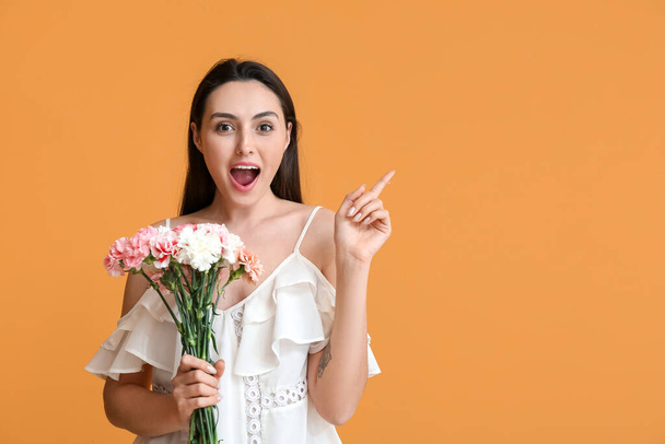 Young woman with carnation flowers pointing at something on color background - Foto, Imagen