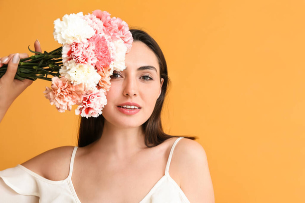 Νεαρή γυναίκα με όμορφα άνθη γαρύφαλλου στο φόντο χρώμα - Φωτογραφία, εικόνα