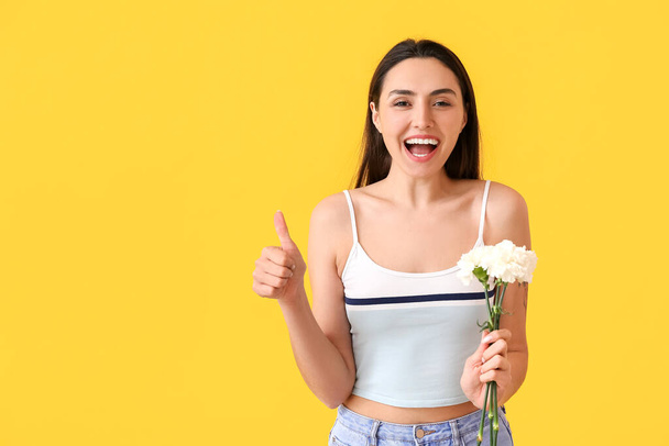 Young woman with carnation flowers showing thumb-up on color background - Photo, Image