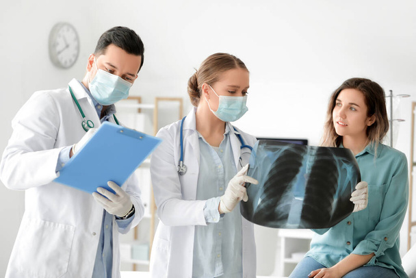 Young doctor showing x-ray image of lungs to patient in clinic - Foto, Imagem