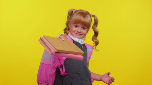 Cheerful schoolgirl kid dressed in uniform showing books on camera, encourages to study together - Photo, Image