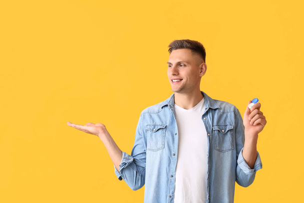 Mladý muž s kontaktními čočkami ukazující něco na barevném pozadí - Fotografie, Obrázek