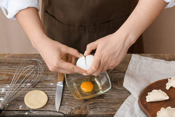 Woman breaking egg into bowl on kitchen table, closeup - Photo, image