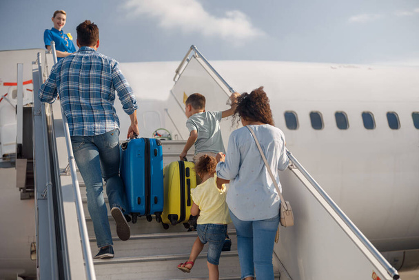 Vue arrière de la famille de quatre personnes montant à bord, embarquant dans l'avion le jour, prêt pour les vacances d'été - Photo, image