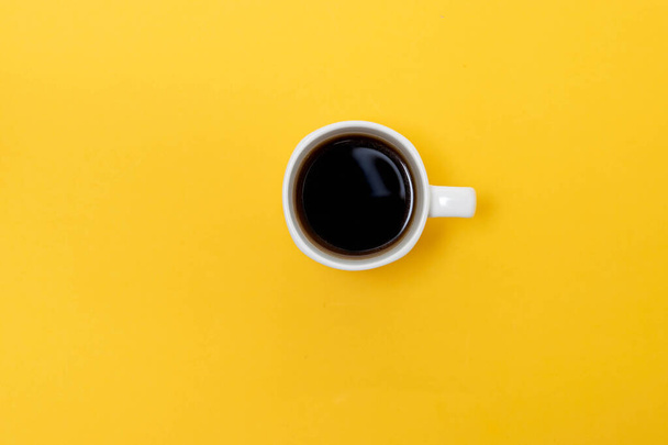 top view of white cup with coffee in isolated yellow background, hot caffeine drink - Photo, Image