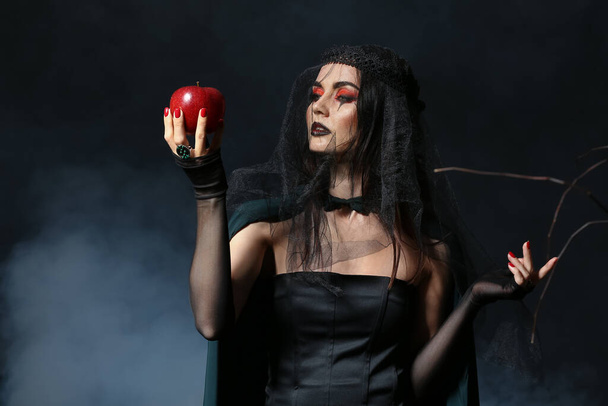 Νεαρή μάγισσα με μήλο σε σκούρο φόντο - Φωτογραφία, εικόνα