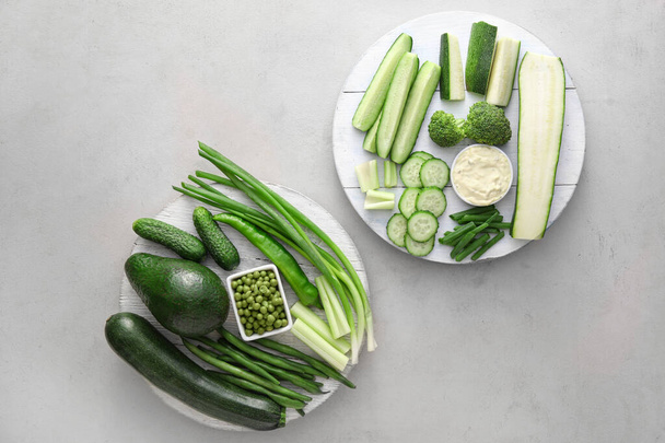 Board with different green vegetables and bowl with sauce on light background - Φωτογραφία, εικόνα