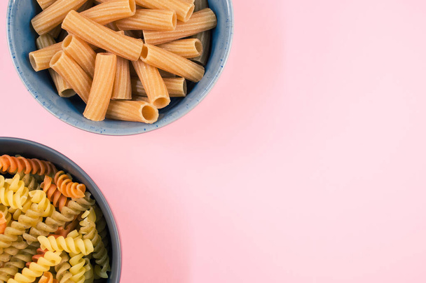 A top view of tri-color rotini and rigatoni pasta on a bowl isolated on pink background - Fotó, kép