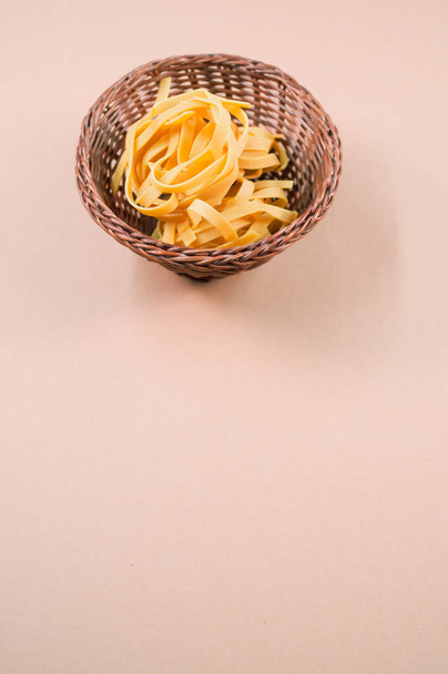 A vertical shot of uncooked fettuccine pasta on a wicker bowl isolated on brown background - Фото, зображення