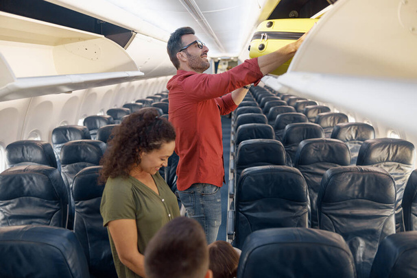 Radosny człowiek rodziny umieszczenie bagażu w przedziale podczas podróży wraz z żoną i małą córeczką samolotem - Zdjęcie, obraz