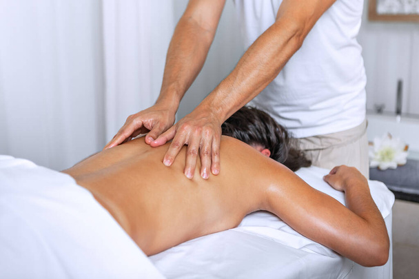 Zrelaksowana młoda kobieta leżąca twarzą na stole do masażu i korzystająca z zabiegowego masażu ciała przez profesjonalnego masażystę w salonie spa. Pojęcie uzdrowiska. - Zdjęcie, obraz