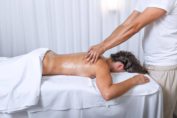 Side view of a latina woman lying face down while therapist doing back massage at health spa. Concept of spa. - Fotó, kép