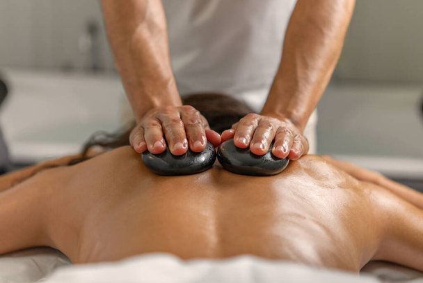Visão traseira de perto de uma mulher latina tendo massagem nas costas com pedras por massagista masculino profissional no spa de saúde. Conceito de spa. - Foto, Imagem