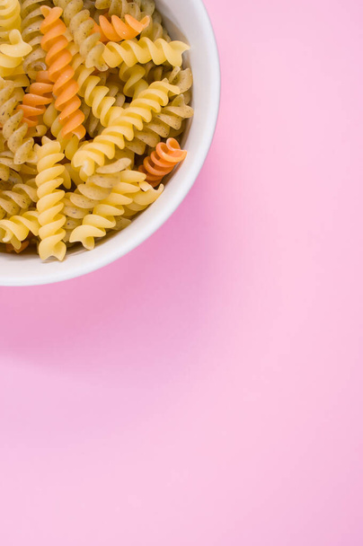 A vertical shot of uncooked tri-color rotini pasta on a bowl isolated on light purple background - Φωτογραφία, εικόνα