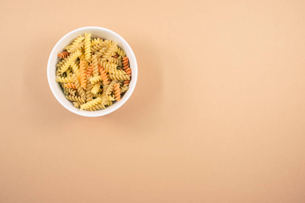 A top view of uncooked tri-color rotini pasta on a bowl isolated on brown background - Foto, Imagem