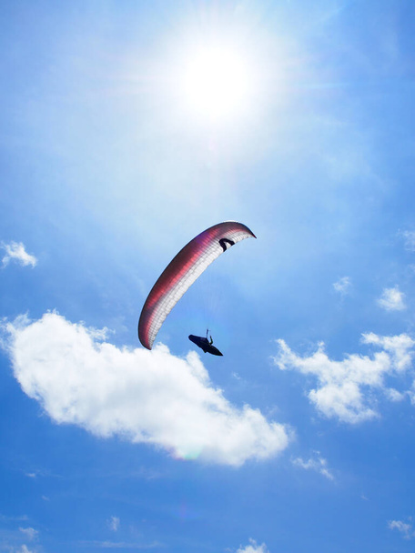 A low angle shot of a person paragliding under a blue sky and sunl - Zdjęcie, obraz