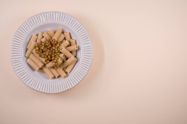 A top view of rigatoni pasta with green peas on a plate isolated on brown background - Foto, afbeelding