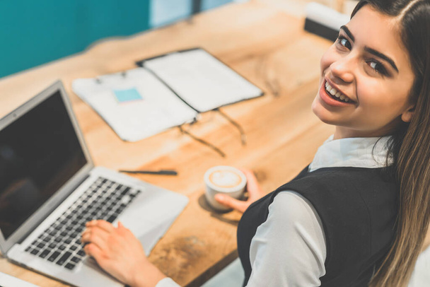 La femme heureuse buvant un café et travaillant avec un ordinateur portable - Photo, image