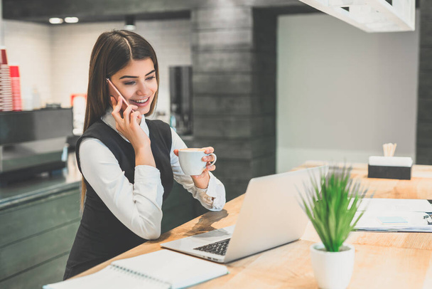 The happy businesswoman with a coffee phones at the desktop - Фото, изображение