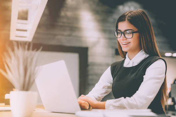 La femme heureuse dans les lunettes de travail avec un ordinateur portable sur le bureau - Photo, image