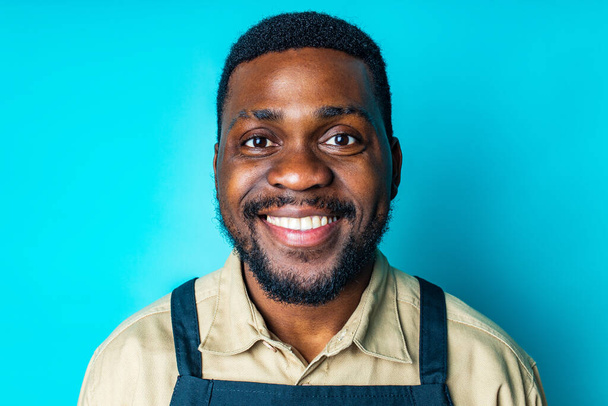 happy latin man in cotton shirt ant black apron in blue studio looking at camera and feeling good - Photo, image