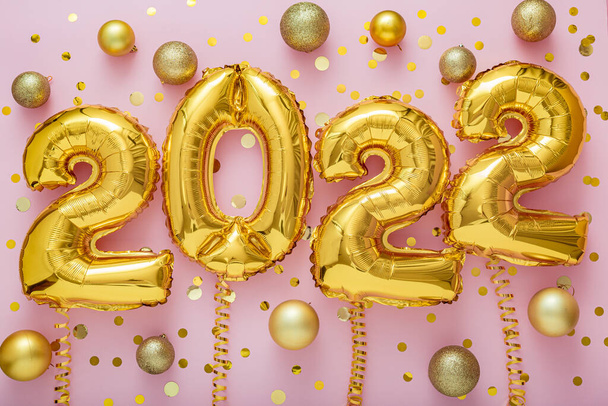 2022 year gold balloons text on ribbons with confetti Christmas gold confetti decor on pink color background. Happy New year 2022 lettering eve celebration - Photo, image