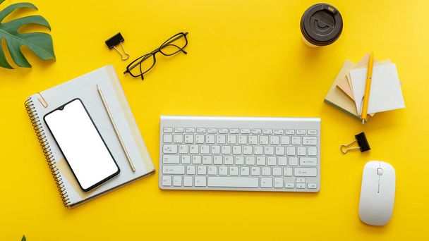 コンピュータキーボードメガネ付きのオフィステーブルデスク、スマートフォンのマウスオフィスは、植物コーヒーカップを提供します。カラフルな黄色の背景にフラットオフィスワークスペース。長いバナーフラットレイアウトモックアップ電話画面 - 写真・画像