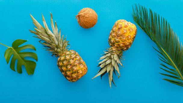Pineapples and palm leaves on blue color summer background. Tropical summer pineapples coconut fruits flat lay composition. long web banner - Photo, image