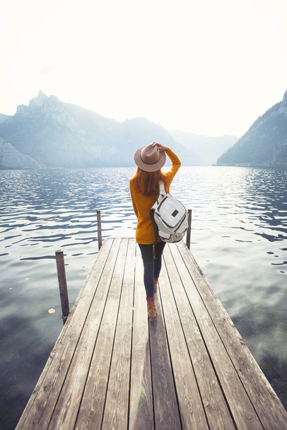 beautiful girl in a hat on the pier at the lake bank and mountains in the backgroun - Foto, Bild