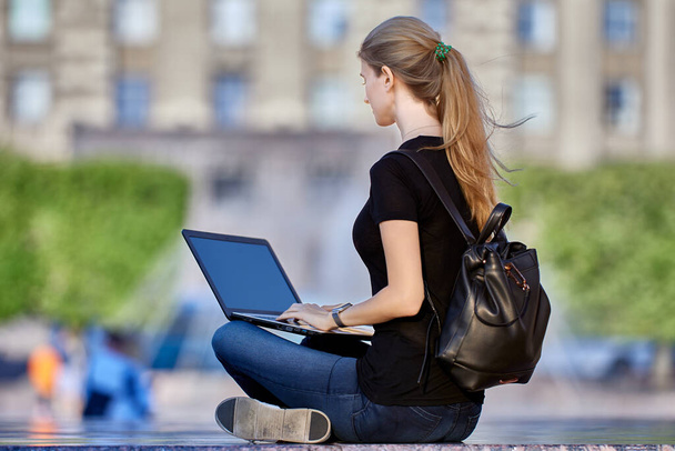 Slender woman in her 30s does remote work on street using laptop. - Foto, Imagen