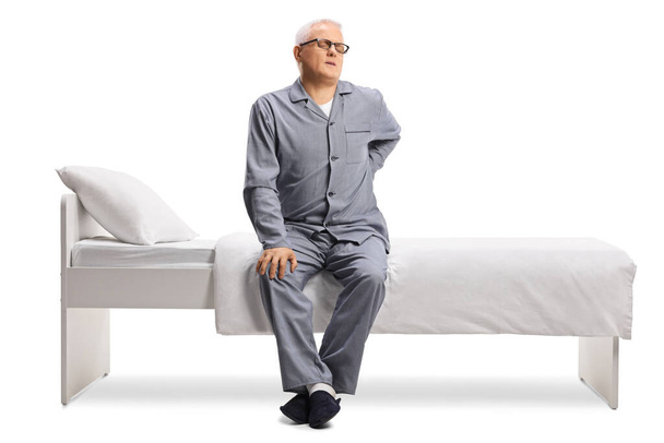 Mature man in pajamas suffering from back pain in a bed isolated on white background - Fotografie, Obrázek