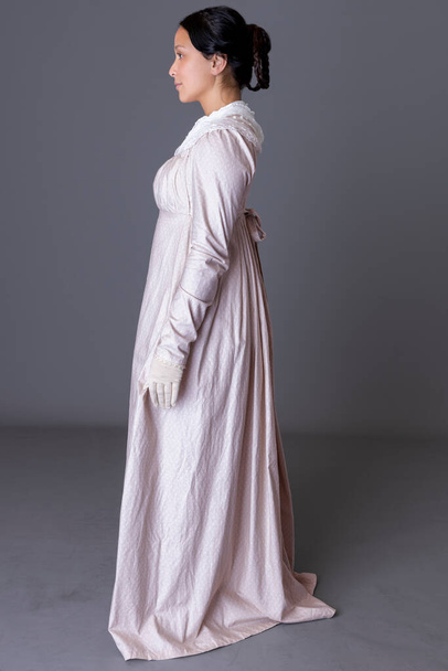 Une femme Regency portant une robe en coton rose avec un châle de modestie en dentelle sur fond de studio gris - Photo, image