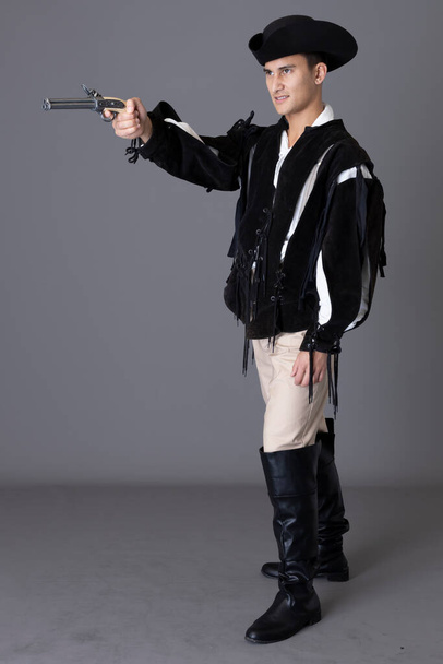 Un personaje pirata sosteniendo un arma contra un fondo gris - Foto, Imagen