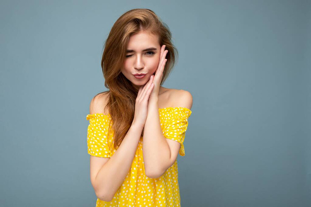 Νεαρή όμορφη σκούρα ξανθιά γυναίκα με ειλικρινή συναισθήματα που απομονώνονται στο παρασκήνιο τοίχο με αντίγραφο χώρου φορώντας κομψό καλοκαιρινό κίτρινο φόρεμα και δίνοντας φιλί. Χαριτωμένο - Φωτογραφία, εικόνα