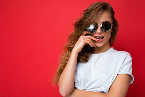 Closeup photo shot of beautiful sexy happy young blonde woman wearing casual clothes and stylish sunglasses isolated over colorful background looking at camera - Fotografie, Obrázek
