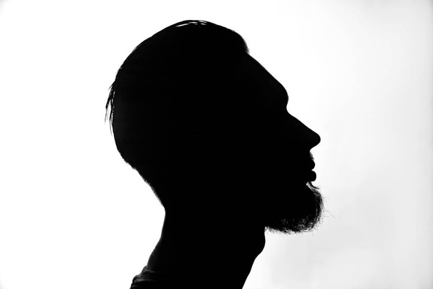 The silhouette of a young man with a stylish hairstyle and beard on a white background. - Foto, Bild
