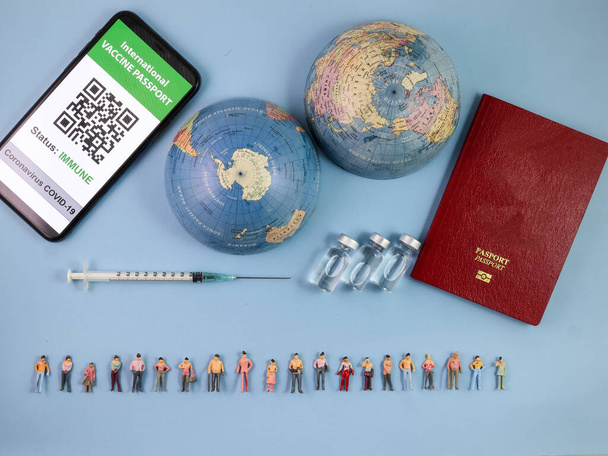 Miniatűr emberi alak figura férfi női baba sor vakcina útlevél digitális papír könyv üveg orvosi injekció fecskendő tű világ térkép világ határ másolás szöveg jel hely kék papír háttér - Fotó, kép