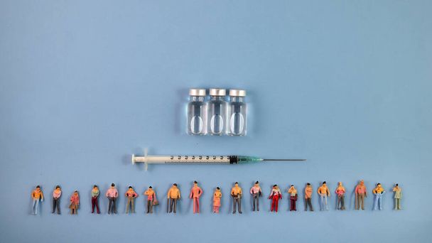 Miniatűr emberi alak figura férfi női baba sor vakcina palack orvosi injekciós fecskendő tű határ másolás szöveges jel helyet kék papír háttér - Fotó, kép