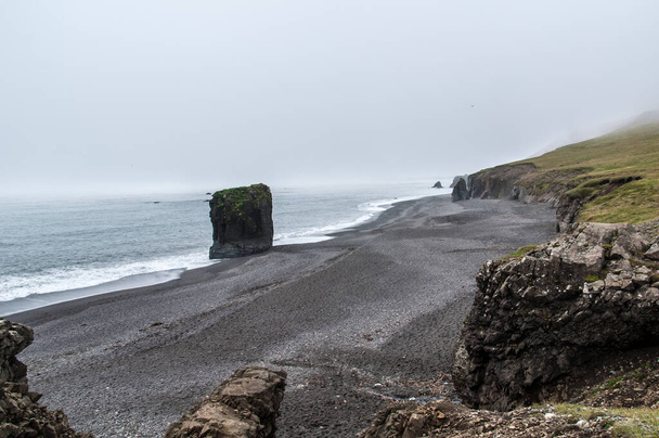 A beautiful shot of rocky cliffs at a beach in Iceland on a foggy day - Zdjęcie, obraz